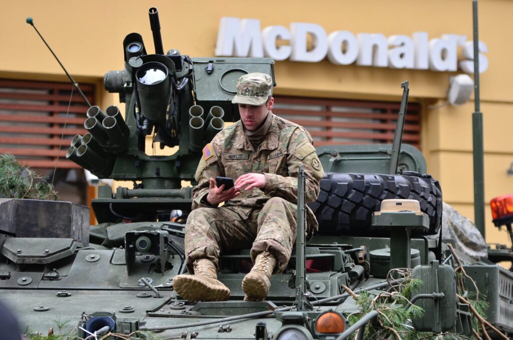 A soldier sits using American weaponry outside McDonalds. Does it get mroe perfect?