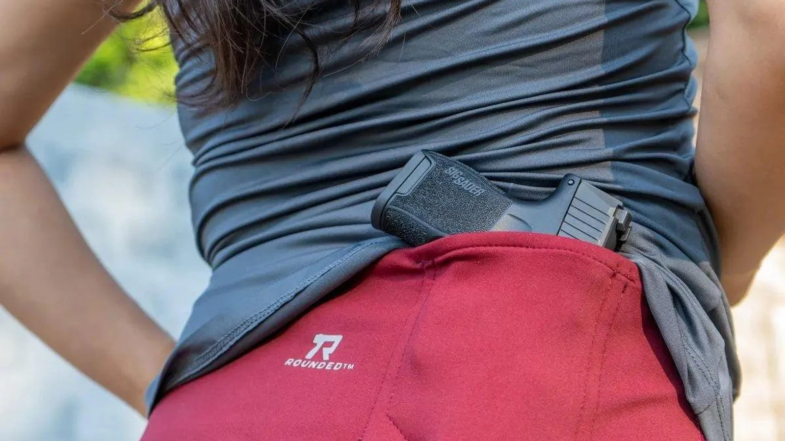 Woman carrying a pistol in the rear pocket of red Rounded concealed carry leggings