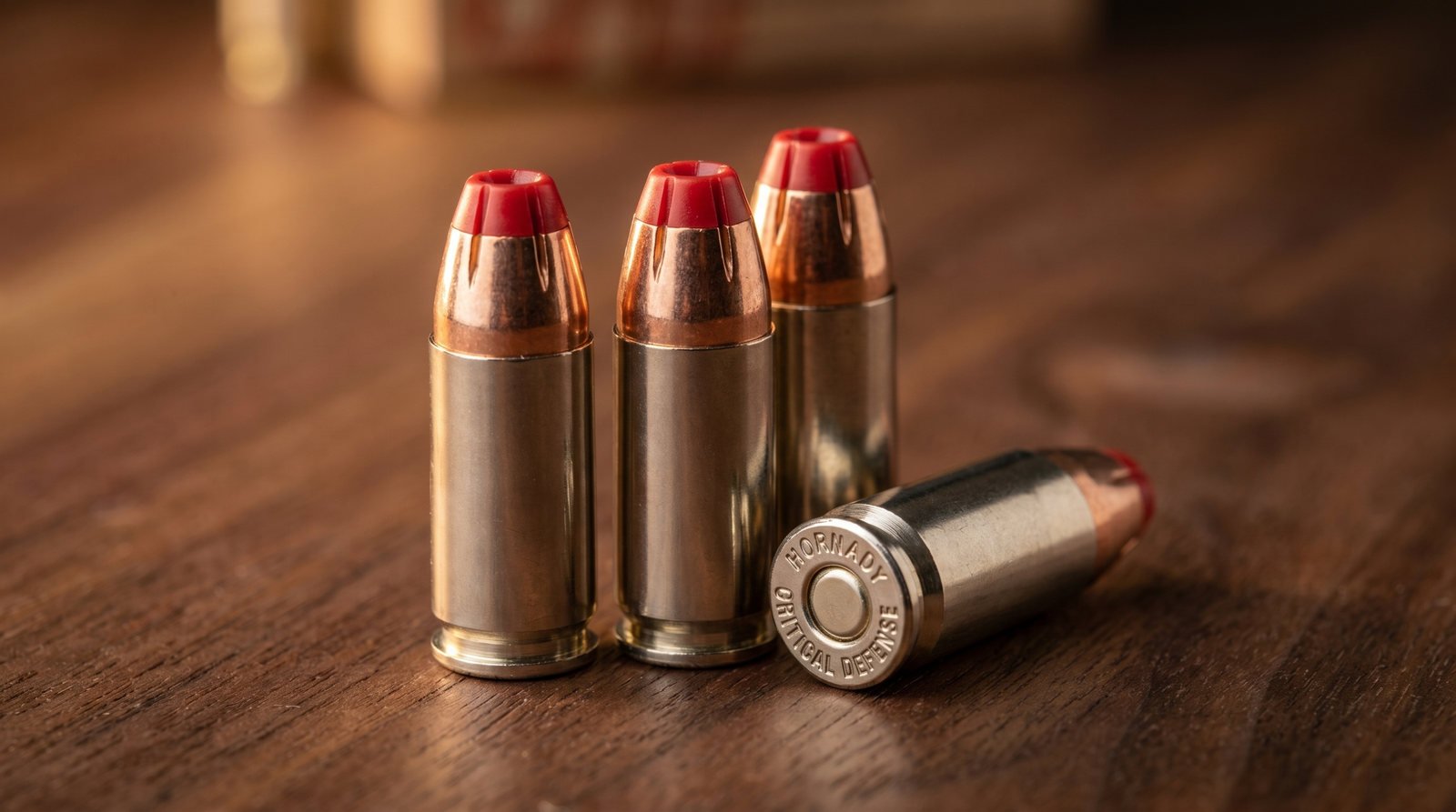 Best 9mm Ammo for Self Defense and Range (2026) 38 Extreme macro of three Hornady Critical Defense 9mm 115gr FTX cartridges standing upright with the distinctive red polymer Flex Tip clearly visible at each bullet tip on dark walnut surface under warm side-light demonstrating the polymer plug that prevents hollow-point clogging through heavy clothing