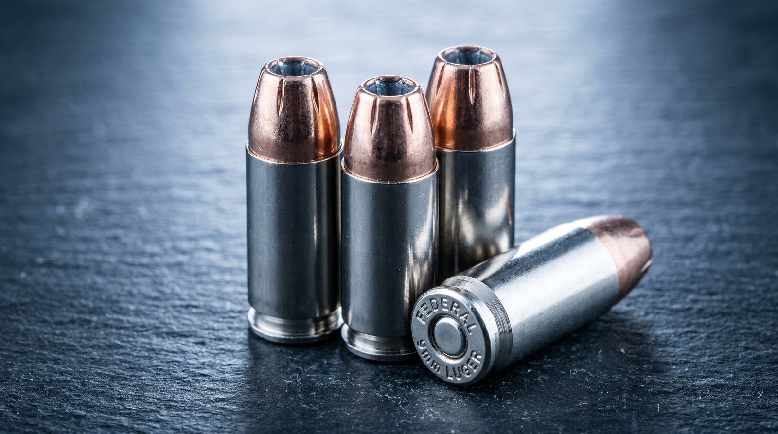 Best 9mm Ammo for Self Defense and Range (2026) 37 Extreme macro studio close-up of three Federal Premium HST 9mm 124gr JHP cartridges standing upright on dark slate with bright nickel-plated brass cases and copper-jacketed hollow-point bullets showing the characteristic Federal HST pre-scored petal jacket design at the exposed JHP cavity