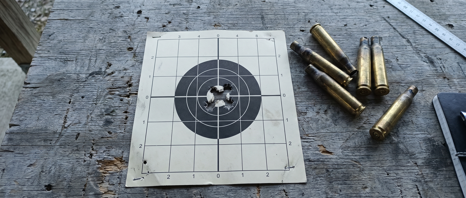 Barrett M82A1 Review (2026): Shooting the Most Famous .50 Cal in the World 15 Paper target showing .50 BMG impact group with spent brass cases on weathered wooden bench