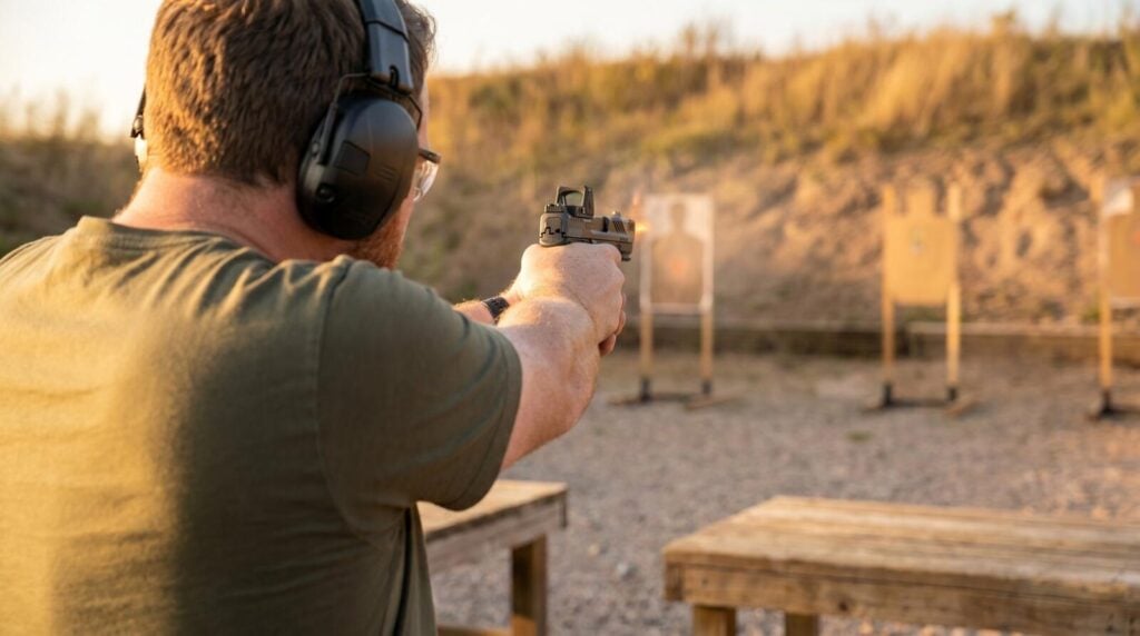 S&W M&P 9 M2.0 Full-Size Review (2026): 500 Round Test of the Duty-Grade 9mm 4 Right-handed shooter in olive tee and ear pro firing the Smith and Wesson M&P 9 M2.0 Full-Size 9mm pistol at an outdoor range with target silhouettes 25 yards downrange and golden hour side-light