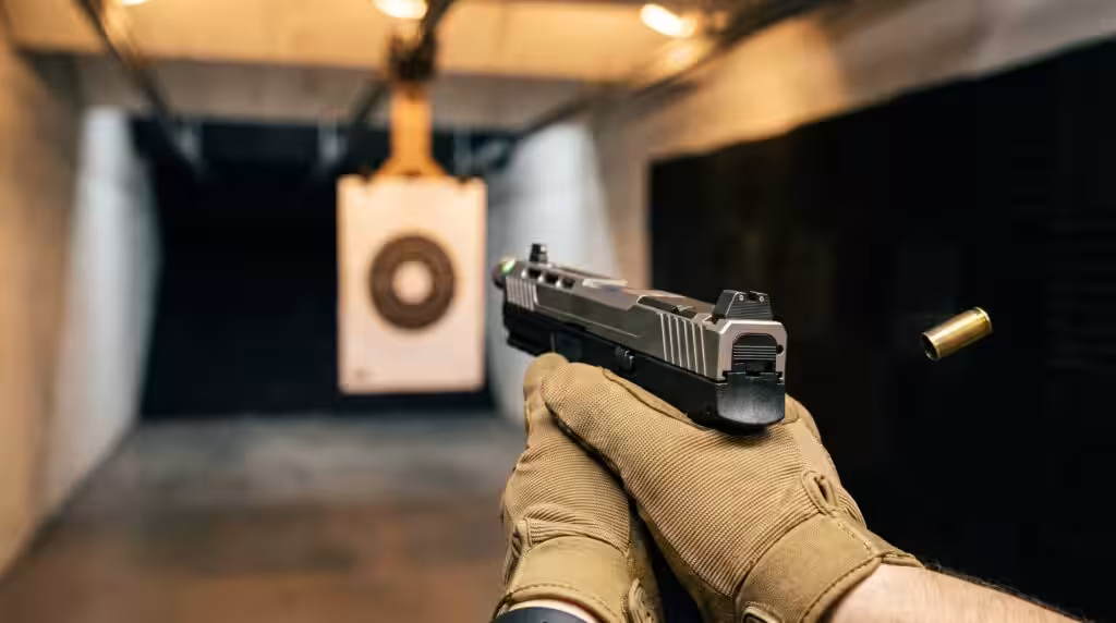 PSA 5.7 Rock Review: 800 Round Test of the Most Affordable 5.7 Pistol (2026) 11 First-person shooter perspective of the PSA 5.7 Rock pointed downrange at an indoor pistol bay target with a brass case ejecting and warm tungsten overhead lighting