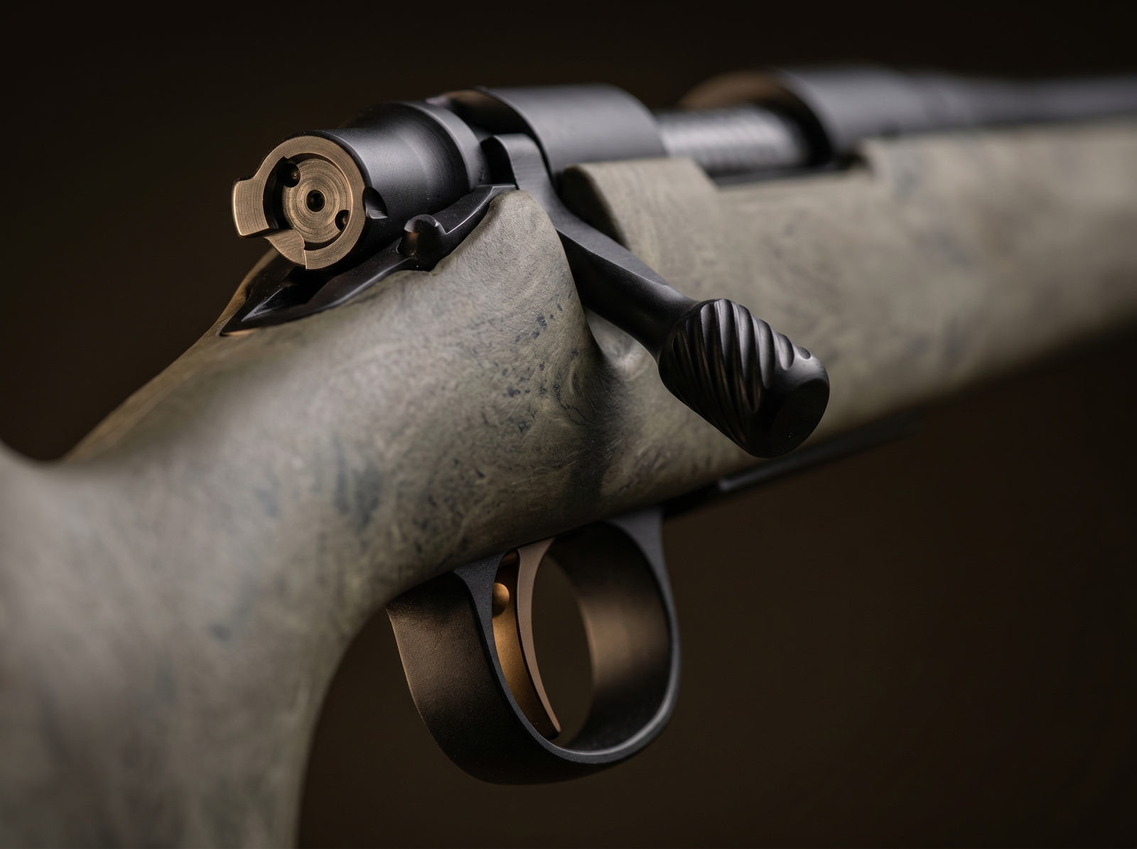 Remington 700 Review (2026): 500 Round Test of the Most Customized Rifle in History 4 Macro detail of the Remington 700 SPS Tactical 2-lug bolt face and bronze X-Mark Pro trigger with spiral-textured bolt knob and tan HS Precision stock in soft focus