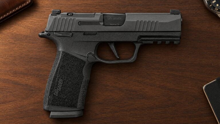 Sig Sauer P365-XMacro 9mm with the 3.7-inch slide lying flat on a walnut desk beside a leather wallet and a wristwatch