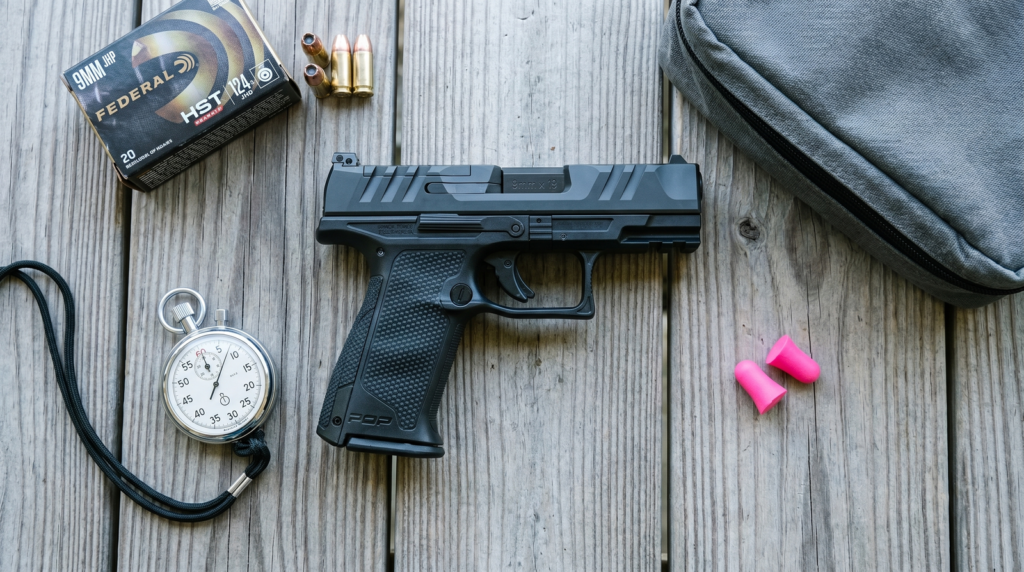 Walther PDP-F Review (2026): 600-Round Test of the First Pistol Engineered for Women's Hands 12 Walther PDP-F top-down flat-lay on weathered cedar shooting bench with Federal HST 9mm 124gr ammo box stopwatch timer pink foam ear pro and folded grey range bag