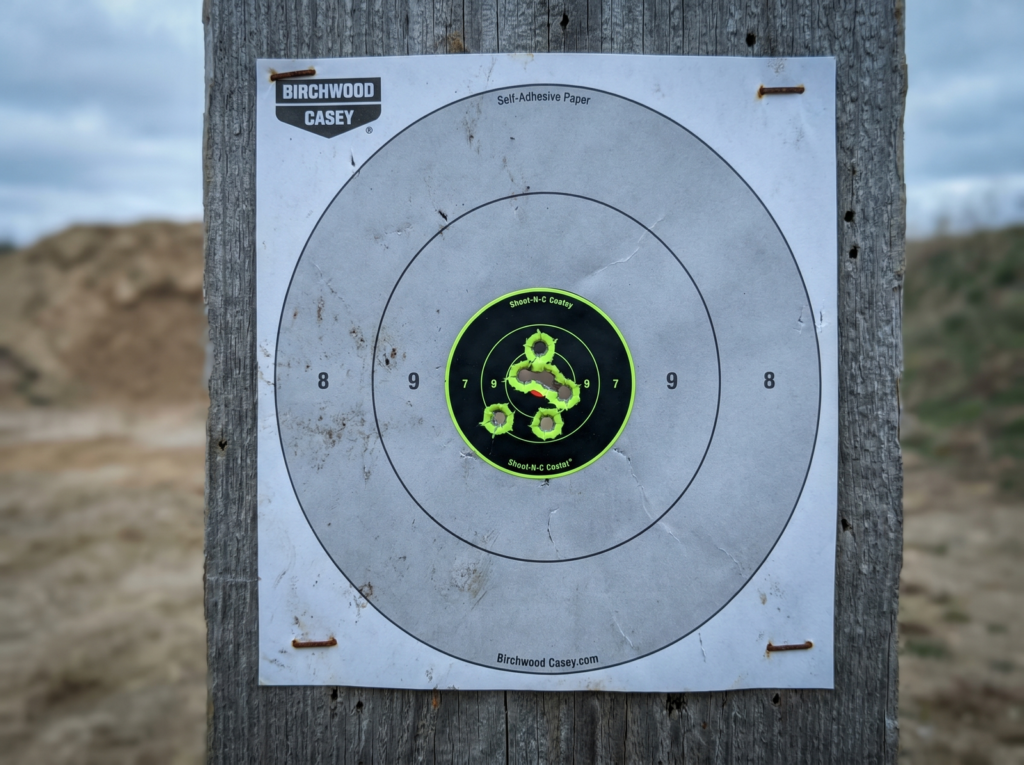 Walther PDP-F Review (2026): 600-Round Test of the First Pistol Engineered for Women's Hands 13 Birchwood Casey self-adhesive silhouette pistol target showing tight five-shot 9mm cluster within center scoring zone with fluorescent green Shoot-N-C reactive impact rings pinned to weathered wooden target backer with rusted staples outdoor range backdrop