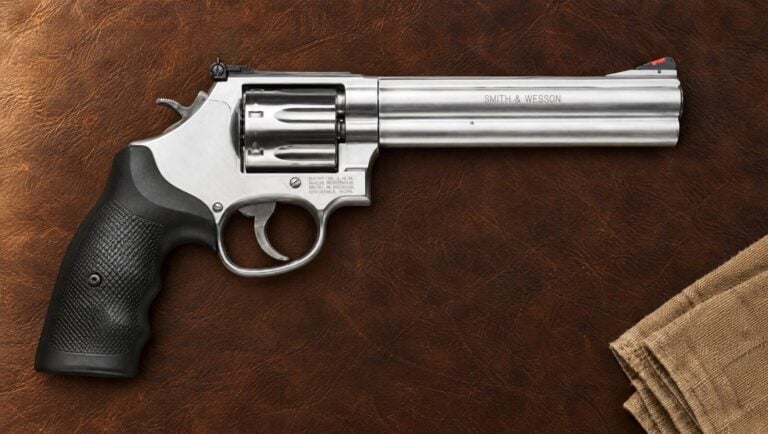 Smith & Wesson 686 Plus 6-inch stainless .357 Magnum revolver lying flat on dark brown leather beside a folded canvas towel