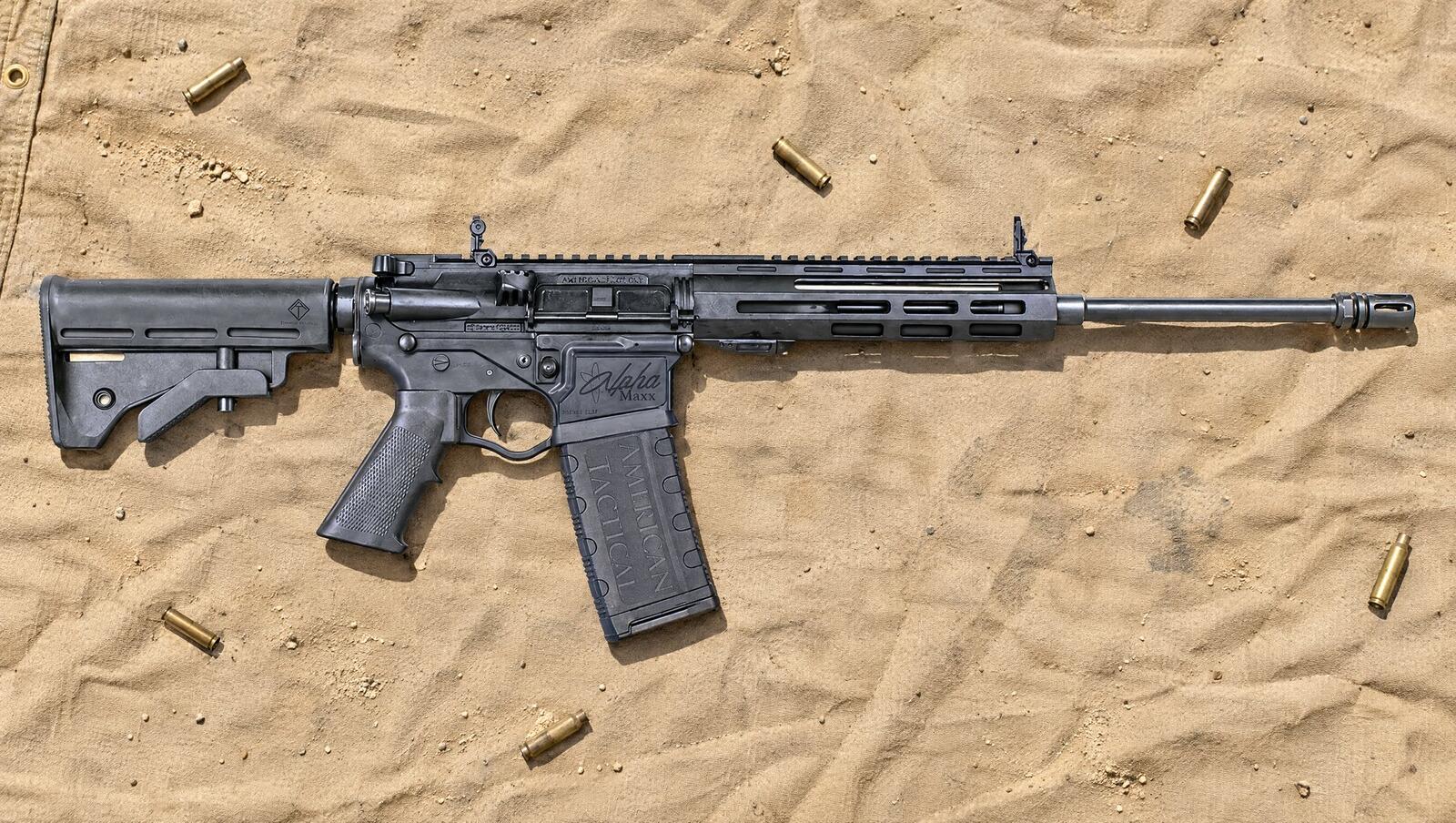 ATI Alpha Maxx polymer AR-15 rifle lying on a tan canvas range tarp in bright sun with spent brass