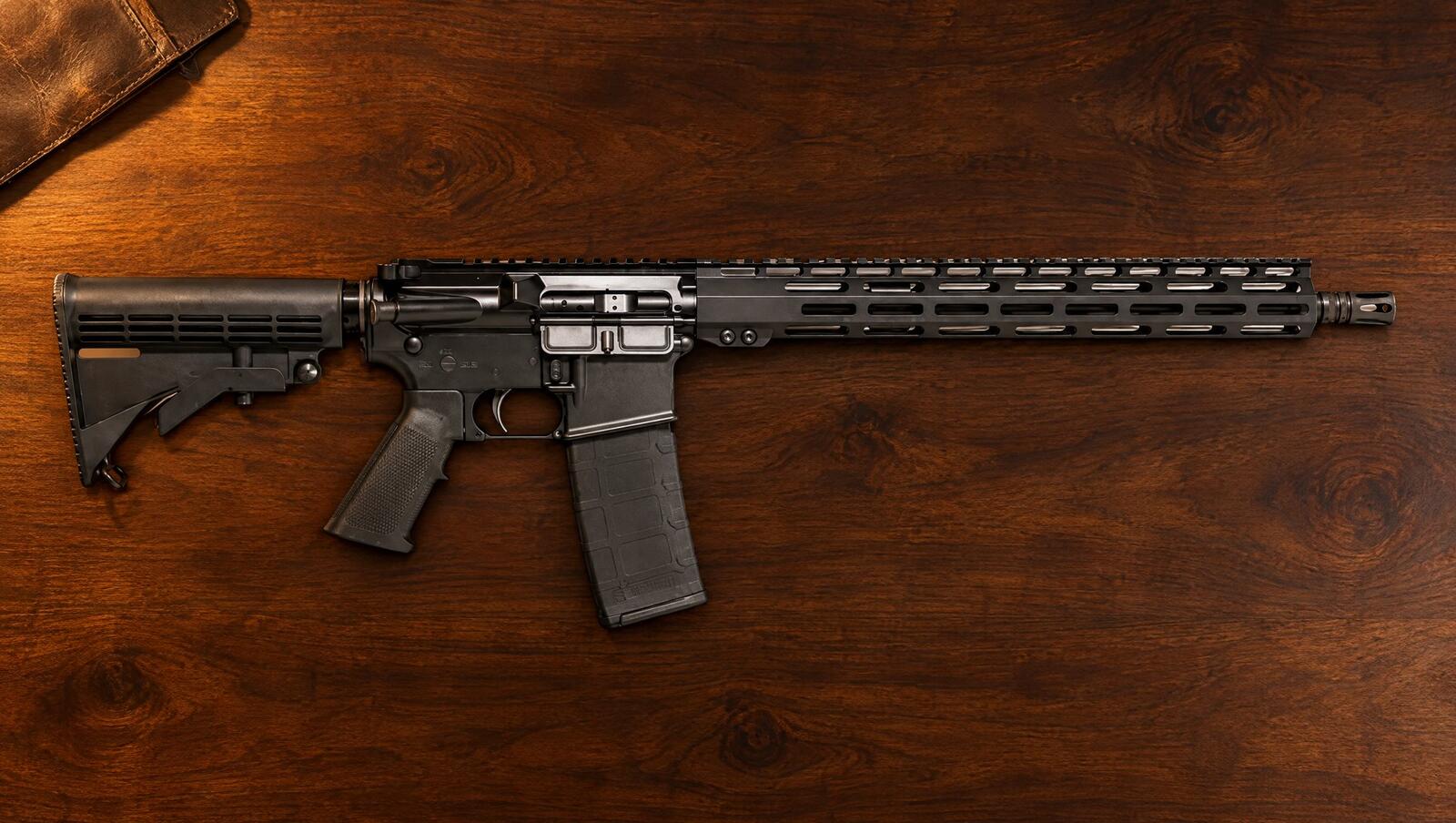 ATI MilSport forged-receiver AR-15 rifle on a dark walnut table in warm lamp light