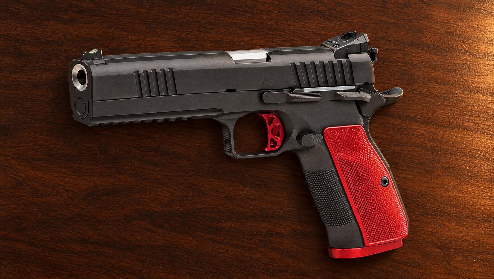 Dan Wesson DWX pistol with red grip panels lying on a walnut desk in warm lamp light