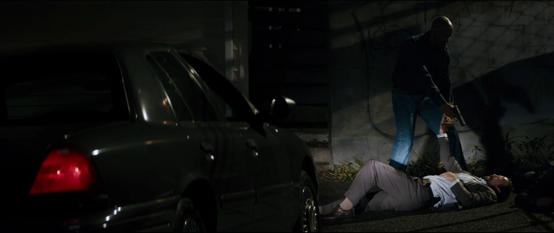 Robert McCall pointing a Glock 17 down at a subdued corrupt detective beside a car in The Equalizer