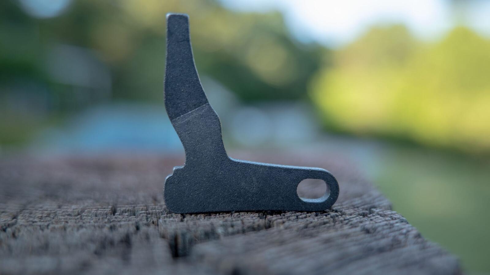 Close-up of a forced reset trigger showing the shaped steel arm that drives the trigger forward