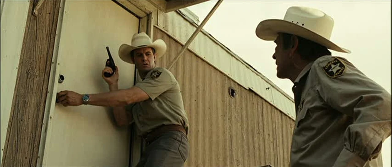 Deputy Wendell holding his Smith and Wesson Model 10 revolver at the trailer door as Sheriff Bell watches in No Country for Old Men