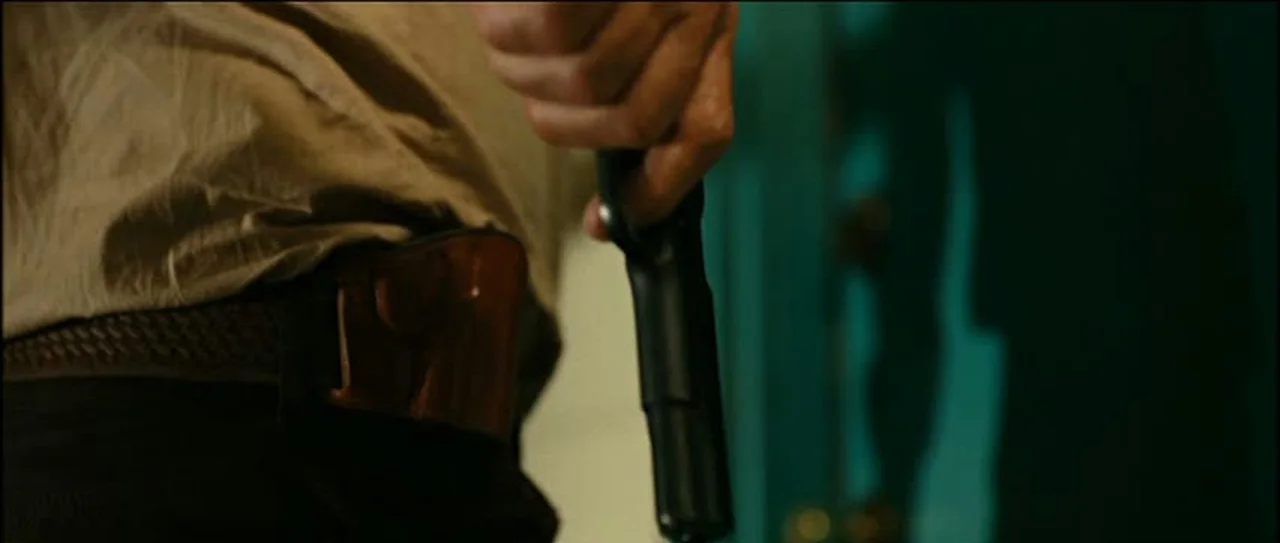 Sheriff Ed Tom Bell holding his Colt Series 70 Government Model pistol beside his belt holster in No Country for Old Men