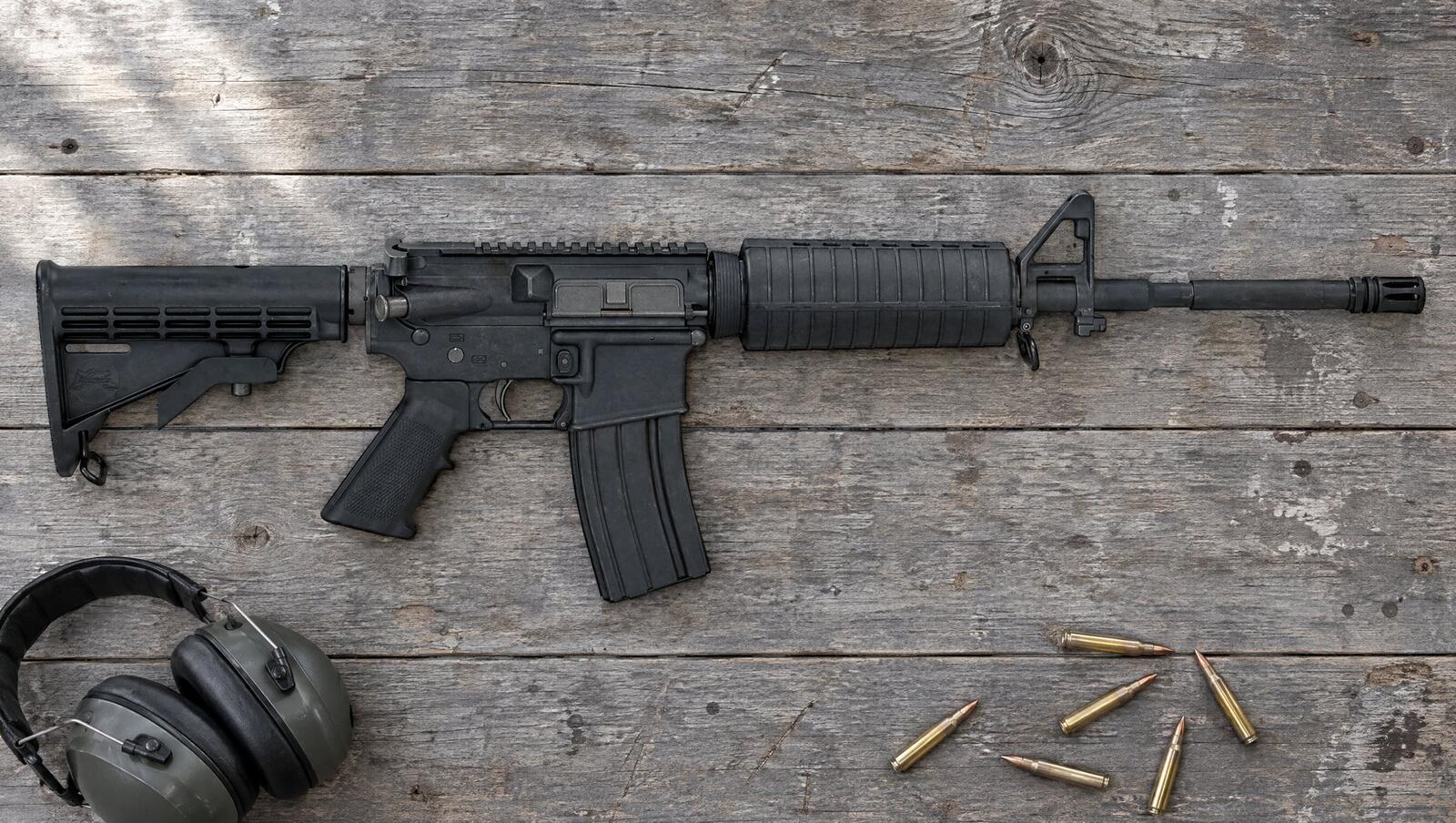 PSA PA-15 Freedom M4 carbine AR-15 lying flat on a gray barn-wood workbench beside ear muffs and loose 5.56 rounds