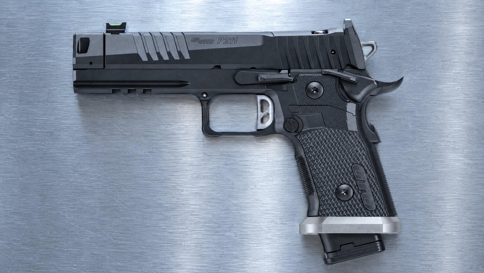 SIG Sauer P211 2011 pistol lying on a brushed steel workbench in cool light