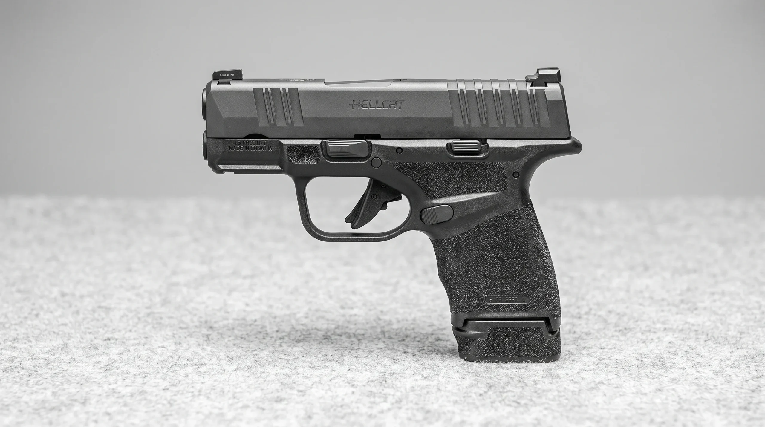 Springfield Hellcat pistol on a light gray wool felt surface with soft top light in a minimalist studio