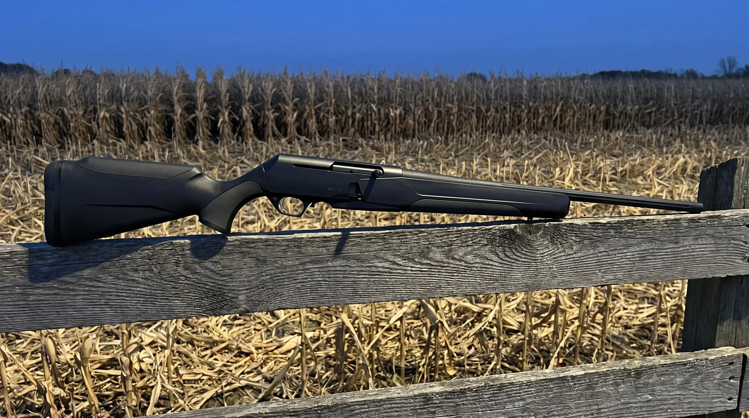 Browning BAR MK4 Hunter Composite rifle on a weathered fence rail at the edge of a cut cornfield at dusk