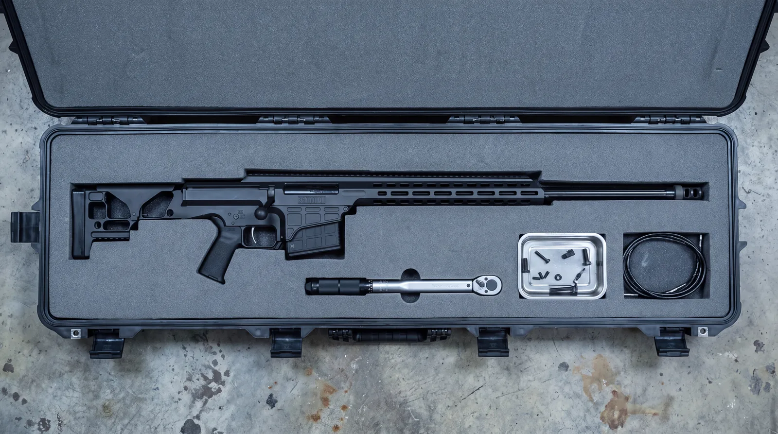 Barrett MRAD SMR black precision rifle photographed from overhead in the foam cutout of an open hard transit case with a torque wrench and parts tray