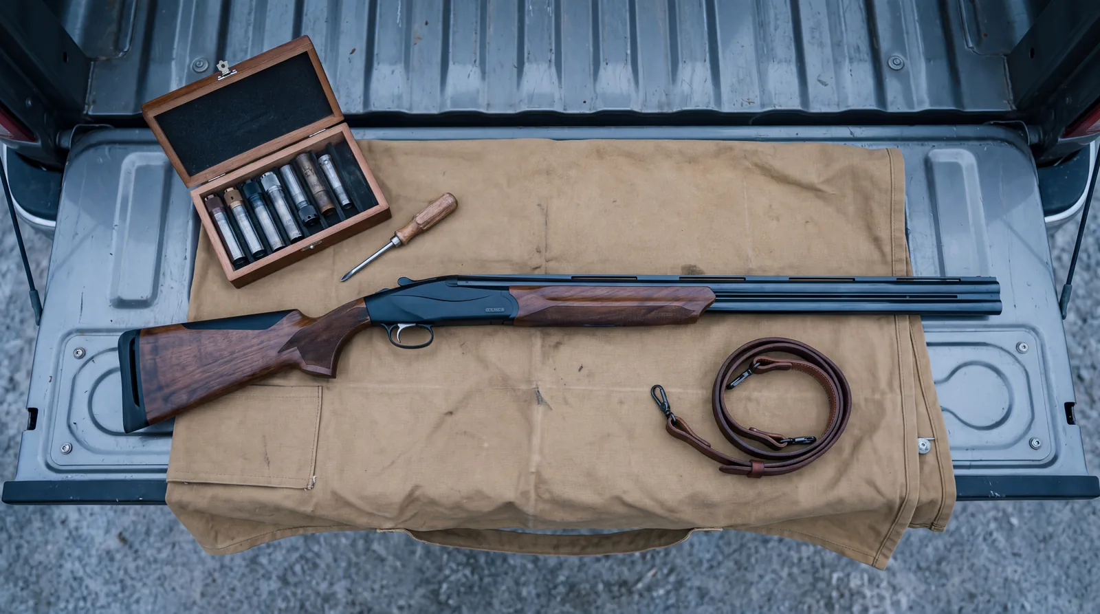 Benelli 828U over and under shotgun photographed from overhead on a canvas tarp on a pickup tailgate with a case of choke tubes and a leather sling