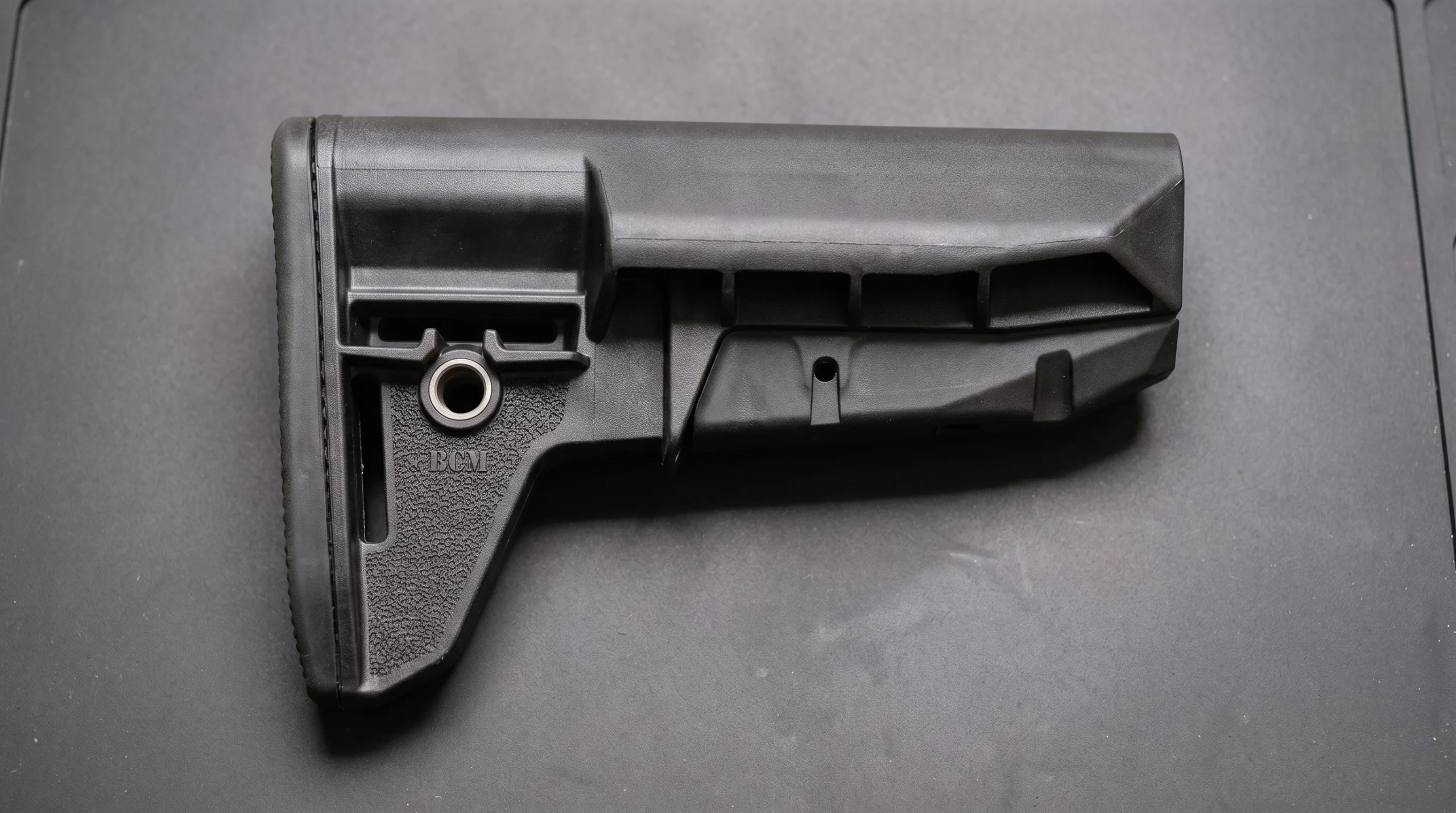 BCM Gunfighter stock on a clean dark gray rubber workbench mat with soft overhead light