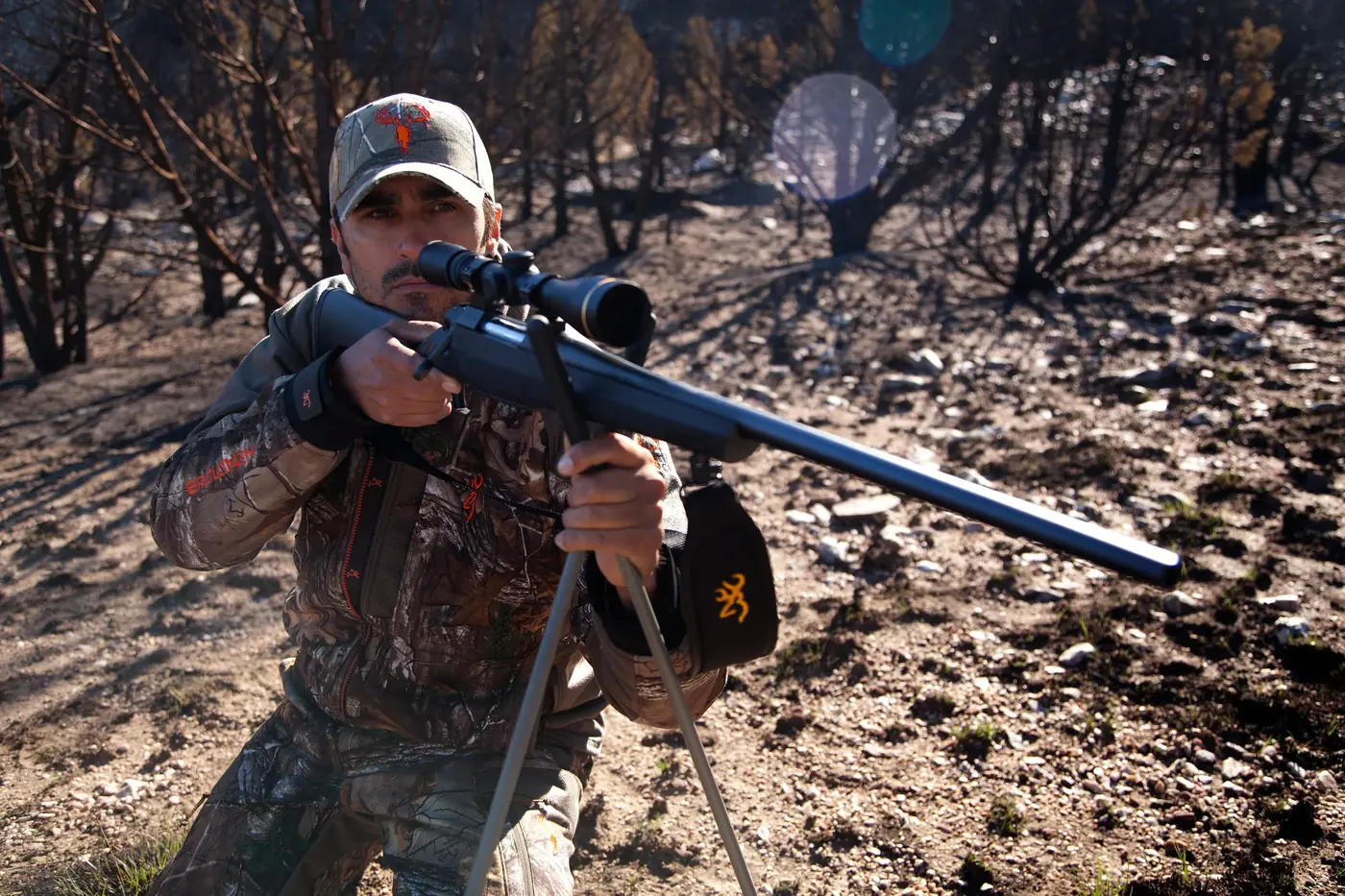 Hunter aiming a scoped Browning AB3 Stalker off shooting sticks in burned timber, Browning photo