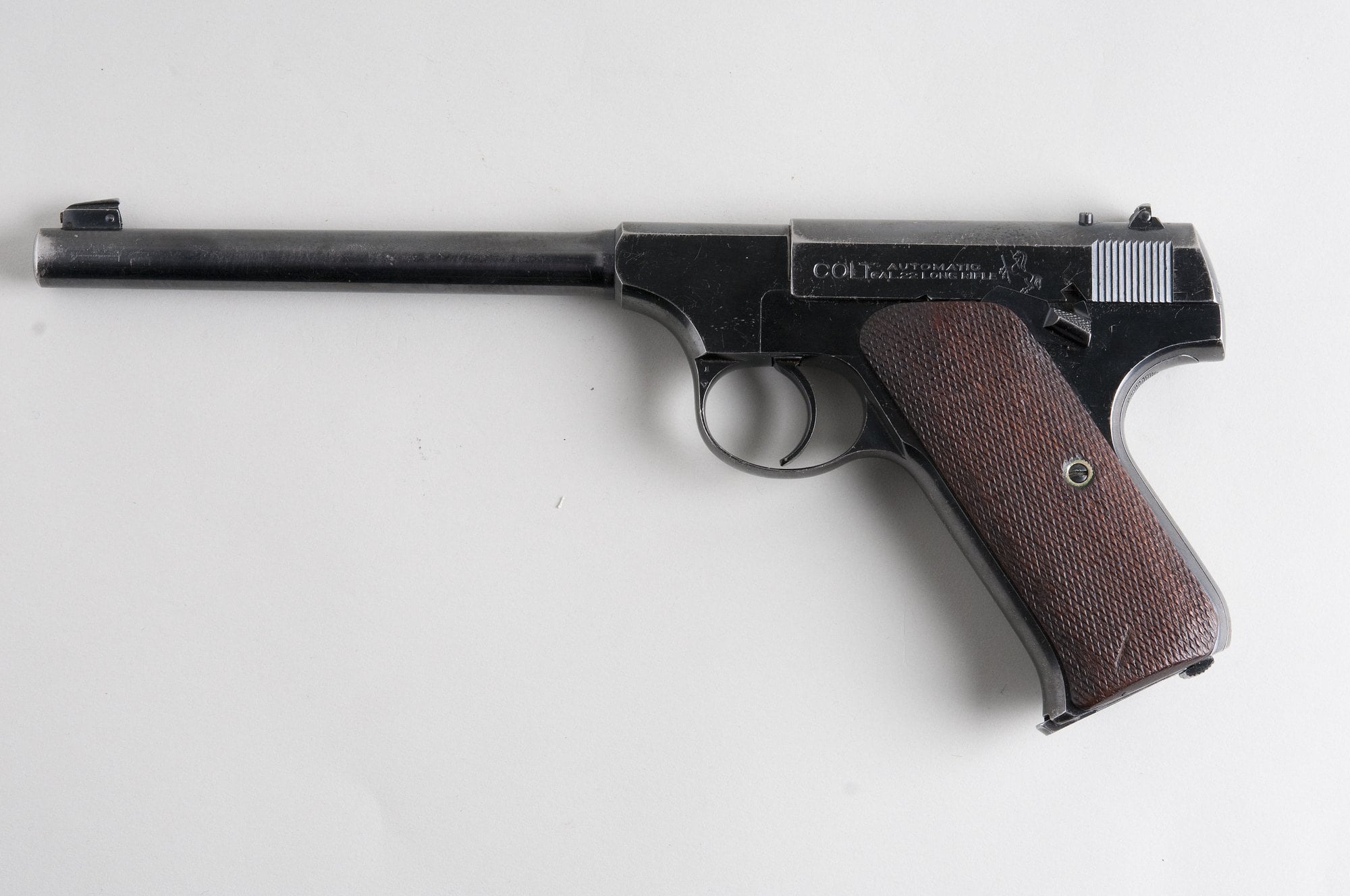 Early Colt Woodsman first series .22 pistol with long round barrel and checkered walnut grips on a plain gray background