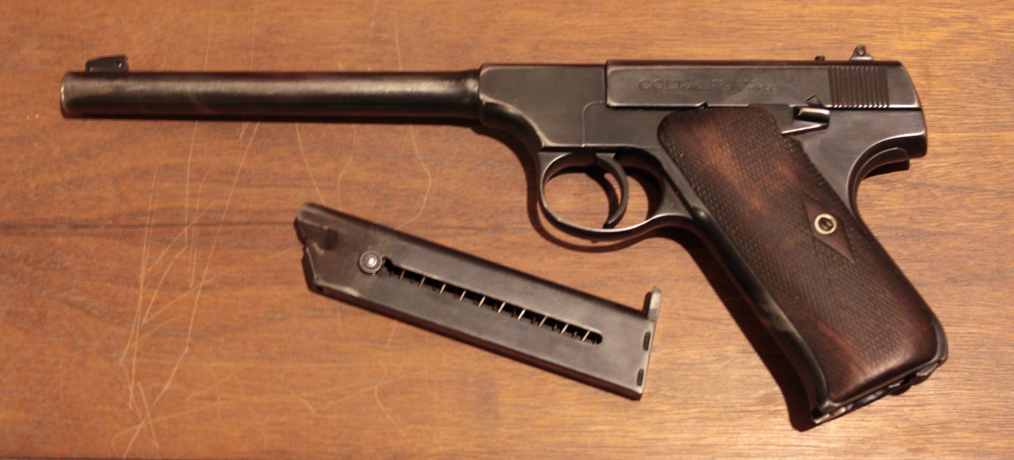 Colt Woodsman first series pistol with its magazine removed, left side view on a wooden table