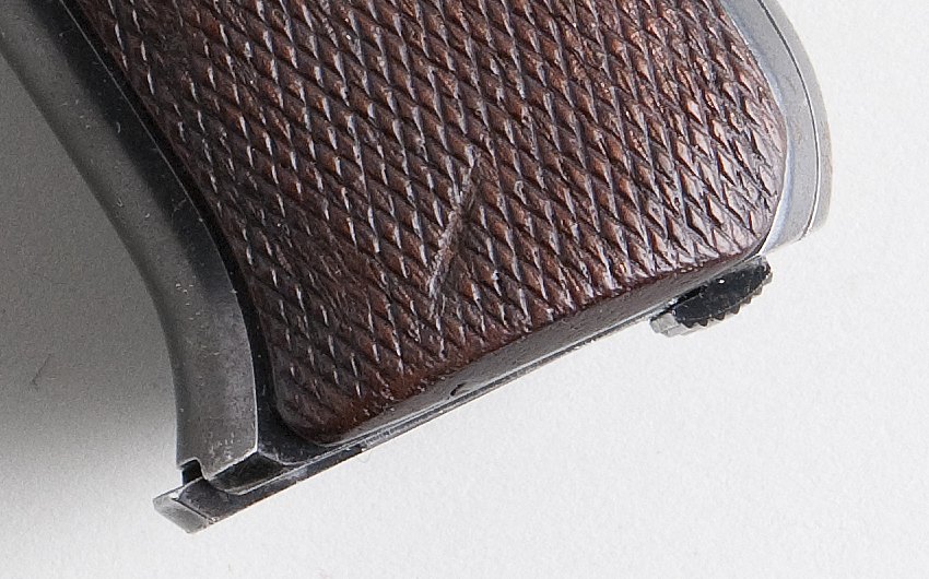 Knurled magazine catch at the heel of a first series Colt Woodsman grip below checkered walnut panels