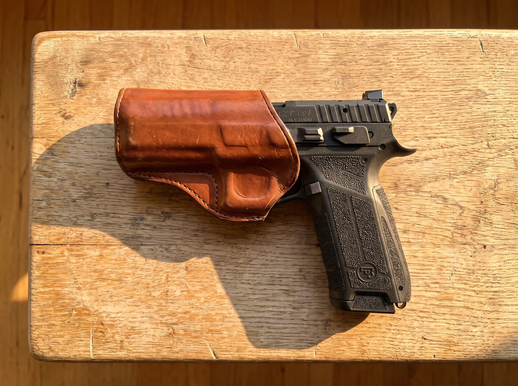 CZ P-09 F Nocturne in a leather holster on a pale oak bench, slide marked CZ P-09 F NOCTURNE