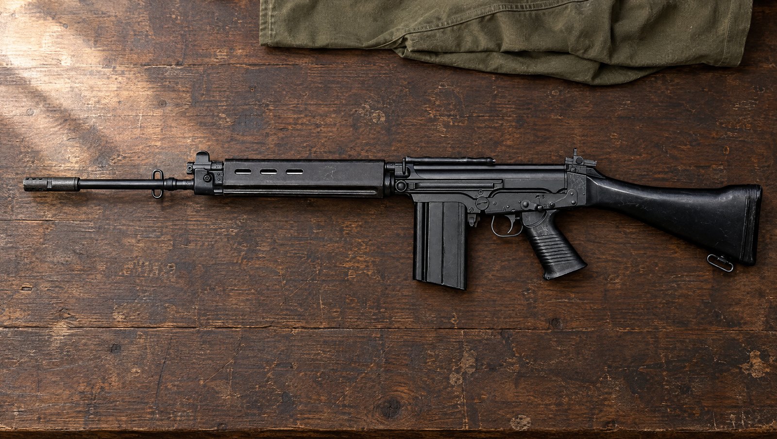 A standard FN FAL rifle with black synthetic furniture and a 20-round magazine lying flat on a weathered oak workbench