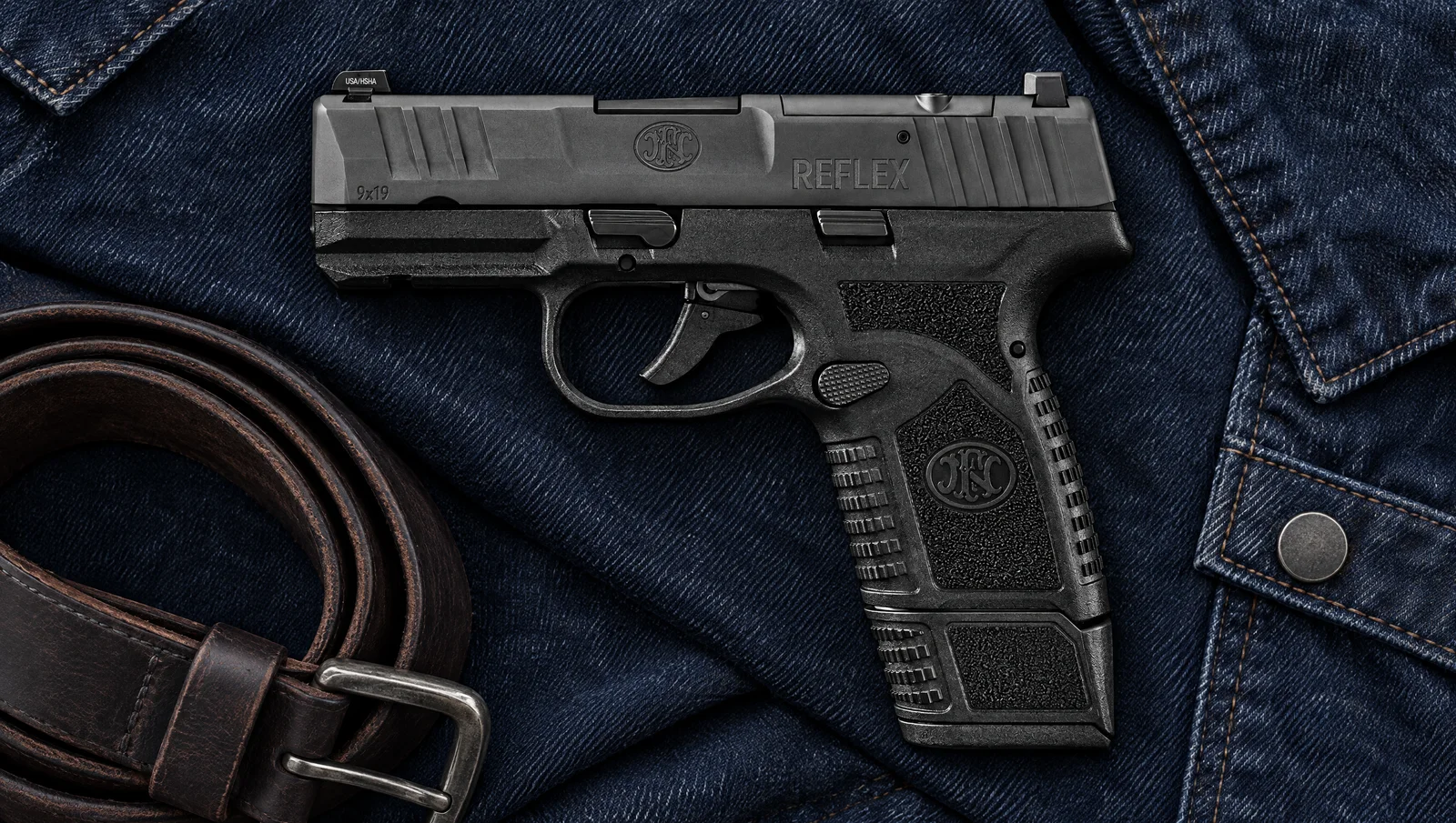FN Reflex MRD 9mm micro compact pistol on a dark denim jacket beside a leather belt