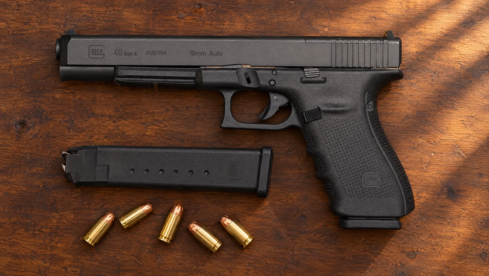 Glock 40 Gen4 MOS 10mm long-slide pistol lying on a walnut workbench beside a spare magazine and five 10mm hollow point cartridges