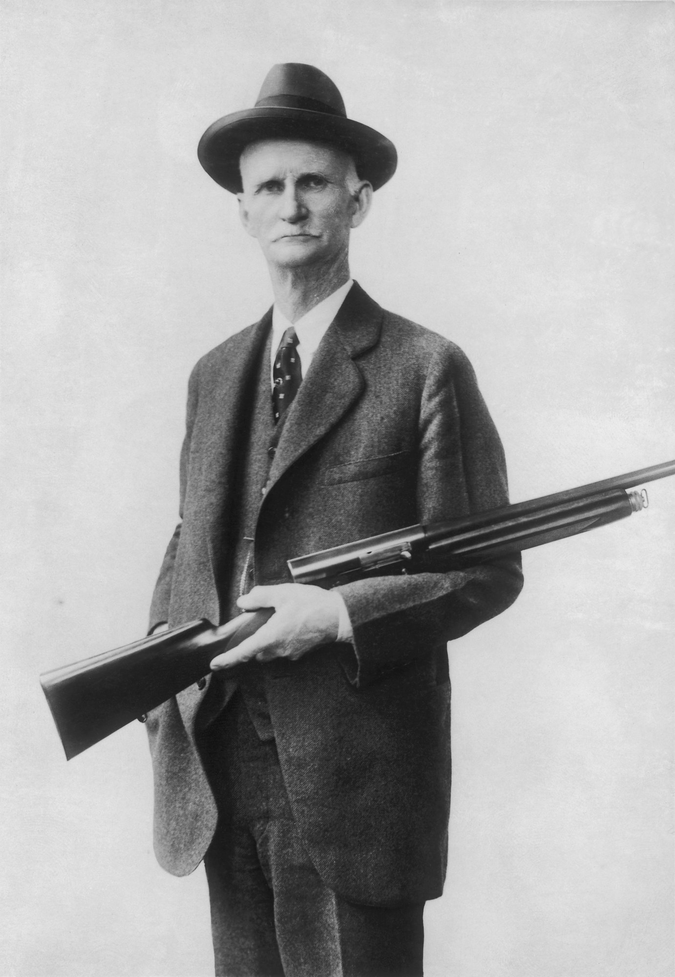 John Moses Browning in a suit and hat holding his Auto-5 semi-automatic shotgun, early 1900s