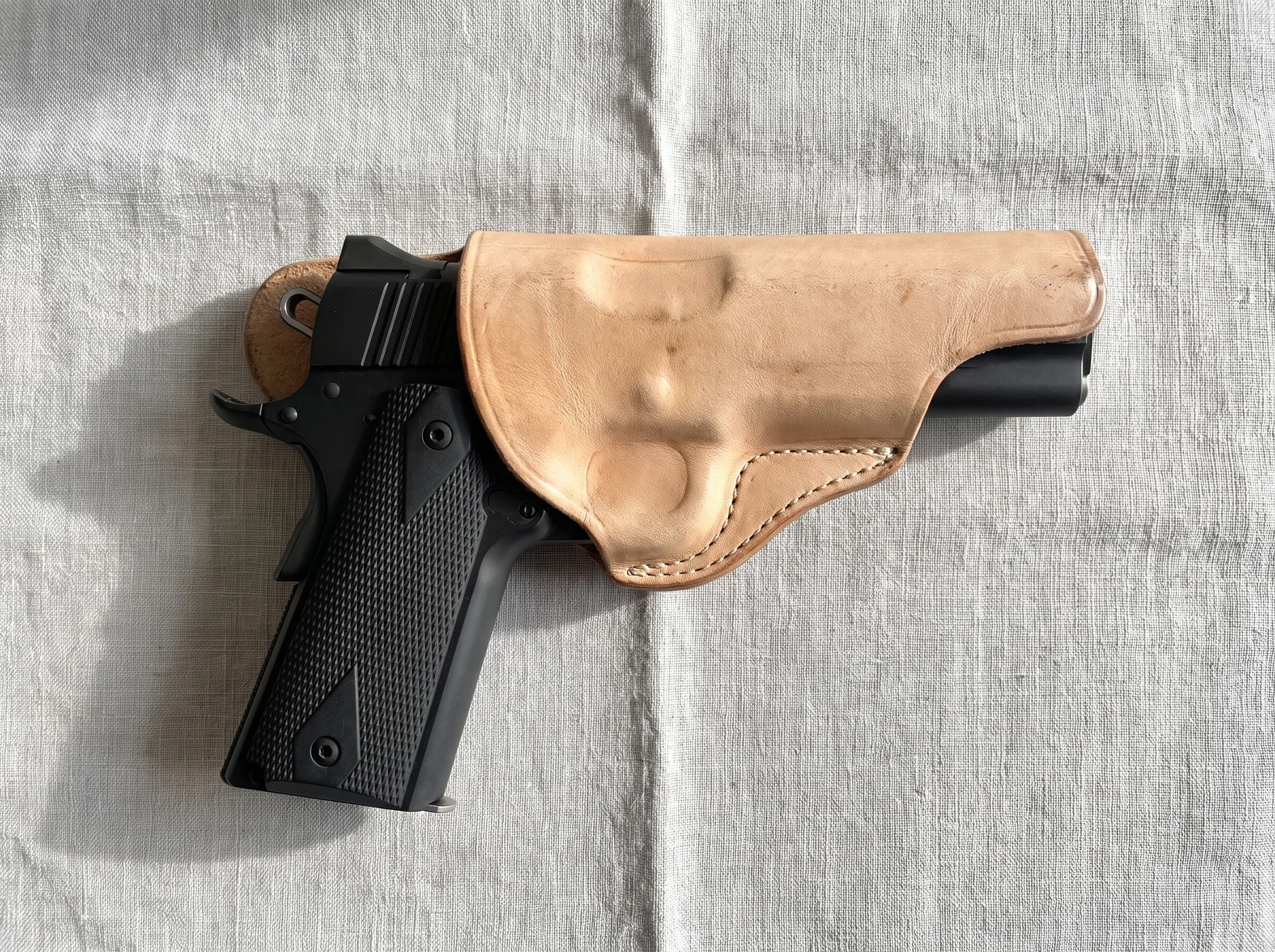 Kimber Custom LW 1911 seated in a tan leather holster on gray linen, seen from above