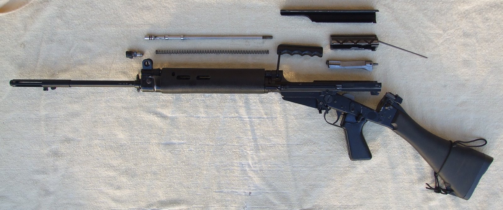 An L1A1 FAL field stripped into its receivers, bolt carrier, bolt, top cover and magazine on a pale cloth