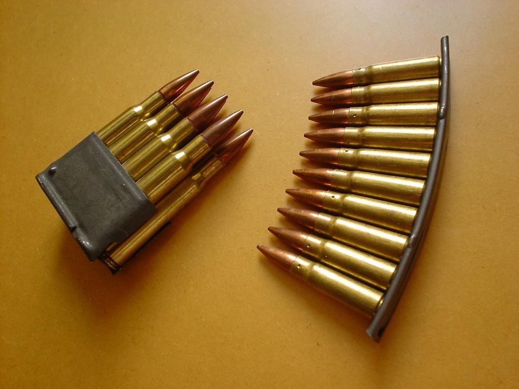 Loaded eight-round M1 Garand en-bloc clip of .30-06 cartridges beside a ten-round SKS stripper clip of 7.62x39 cartridges