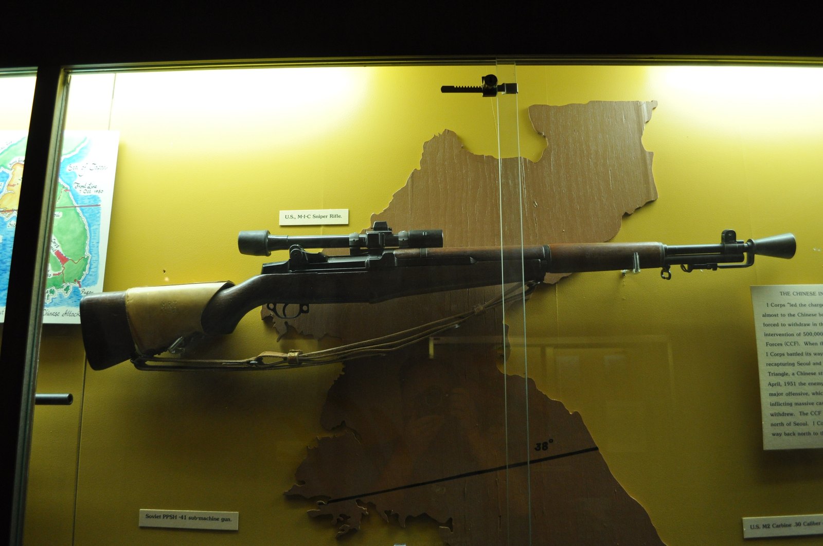 US M1C Garand sniper rifle with scope, flash hider and leather cheek pad displayed in a Korean War museum case