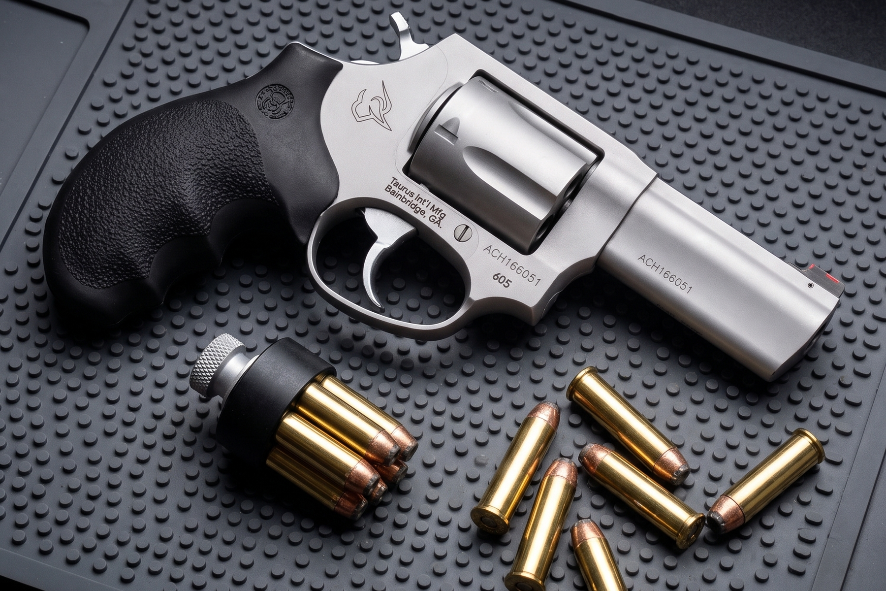 Taurus Defender 605 three inch .357 Magnum revolver on a range mat with a loaded speedloader and loose cartridges