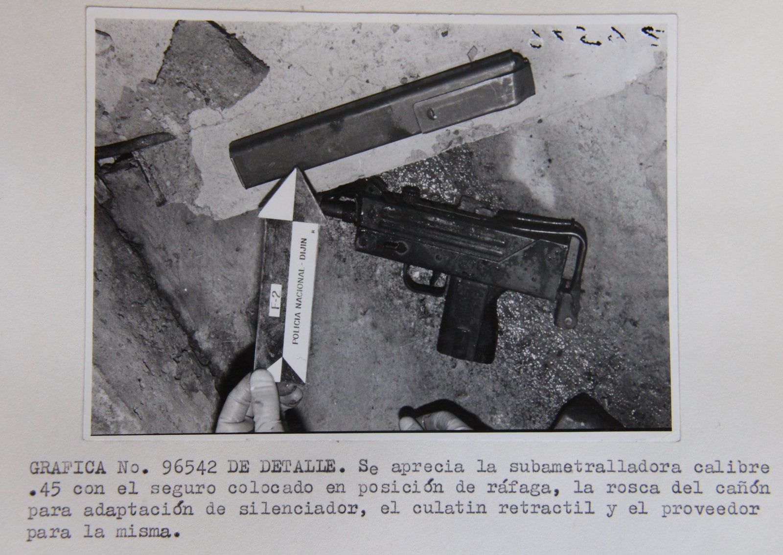 Colombian police evidence photograph of a .45 caliber MAC-10 with its retractable stock and a magazine lying on concrete, with a typed Spanish caption below