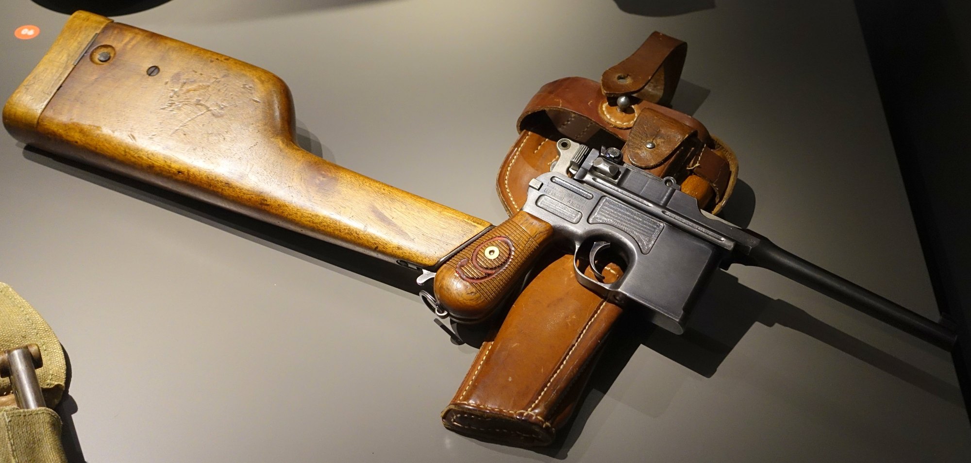 Mauser C96 Red 9 with its wooden shoulder stock fitted to the grip, next to a leather holster rig