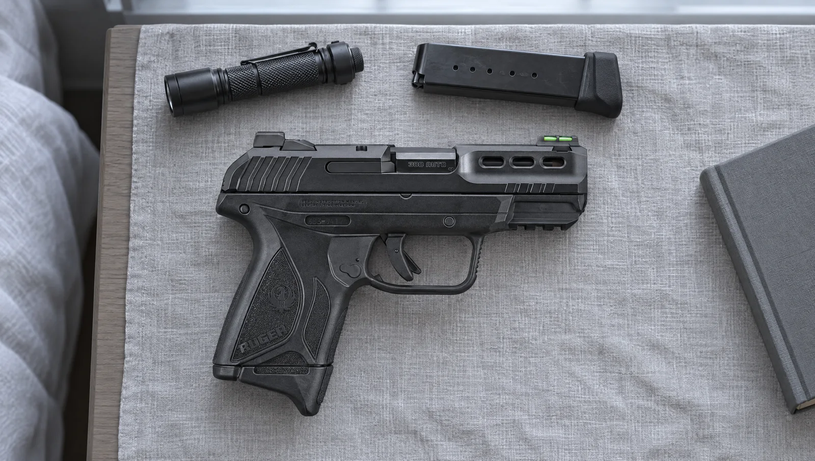 Ruger Security-380 .380 Auto pistol with fiber optic front sight lying on gray linen on a nightstand beside a flashlight and a spare magazine