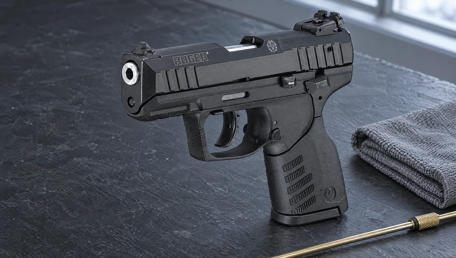 Ruger SR22 pistol standing on a dark slate workbench beside a gray shop towel and a brass cleaning rod