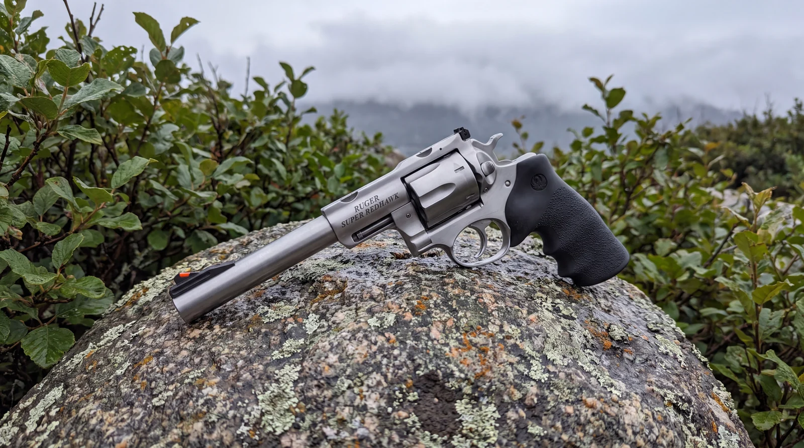 Ruger Super Redhawk .44 Magnum revolver on a lichen covered granite boulder in coastal alder brush under low cloud