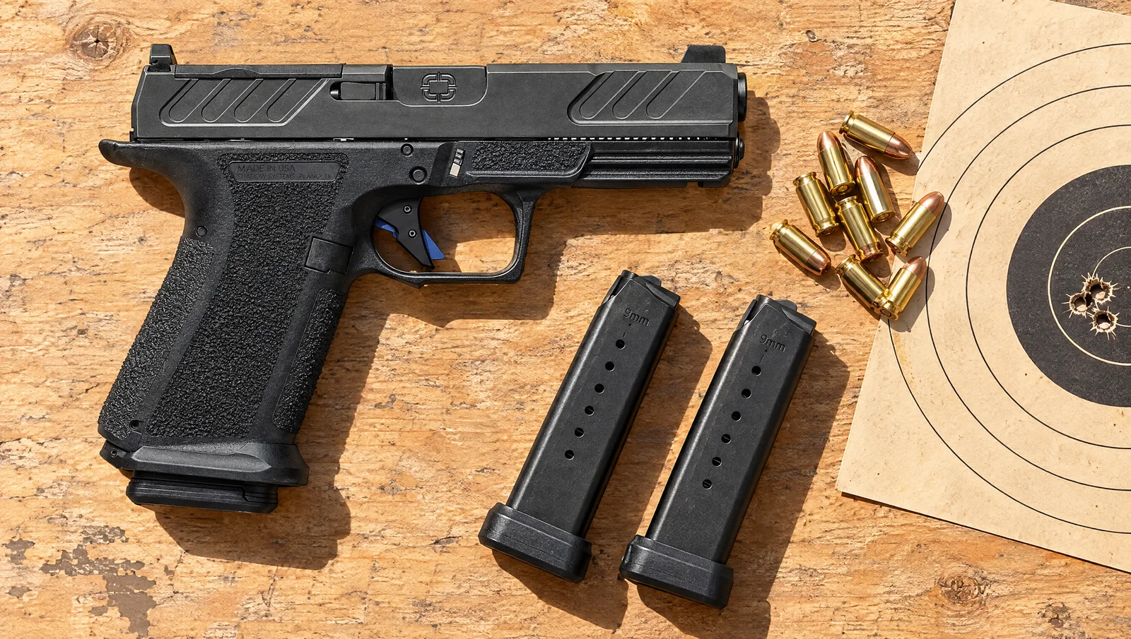 Shadow Systems MR920 pistol on a plywood range bench beside two spare magazines, 9mm cartridges and a paper target