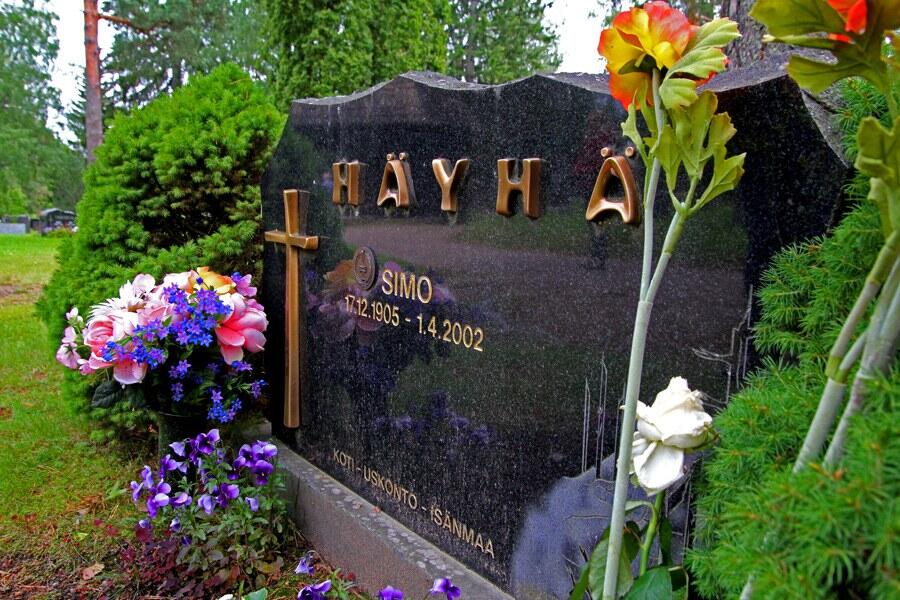 Simo Häyhä's black granite gravestone surrounded by flowers in the Ruokolahti church graveyard