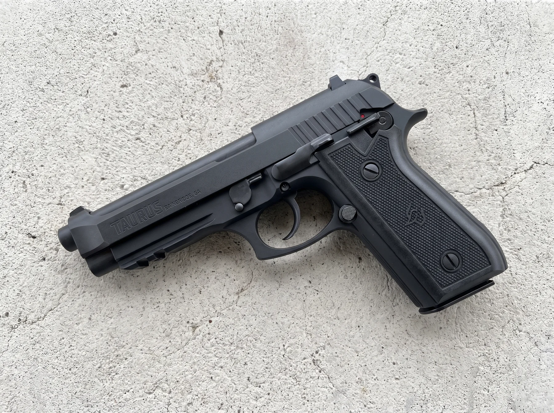 Taurus 92 matte black 9mm with TAURUS slide marking on a gray concrete range bench