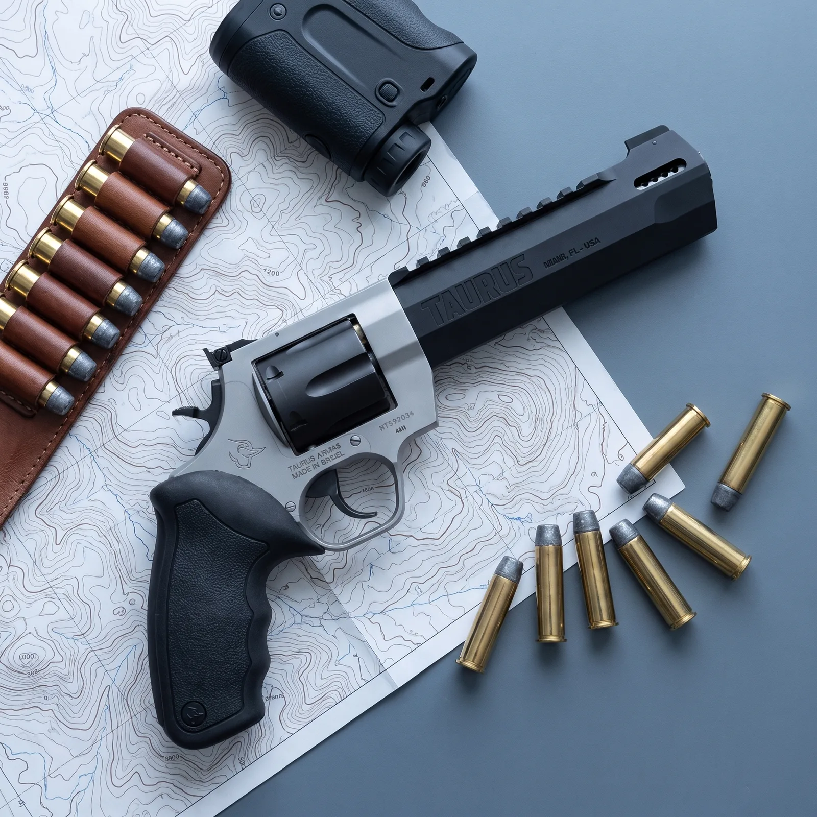 Taurus Raging Hunter revolver on a topographic map with a rangefinder, cartridge slide and loose .44 Magnum rounds
