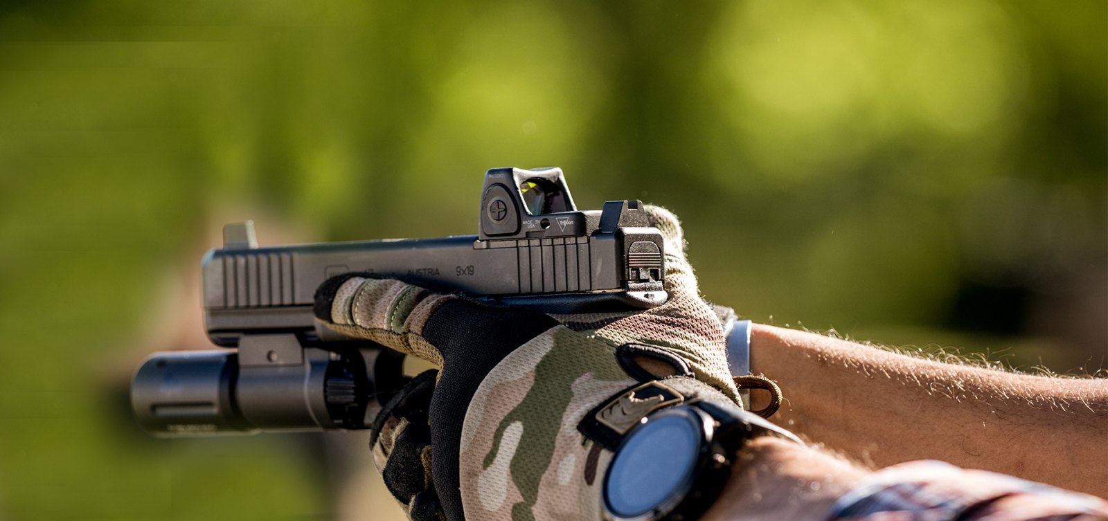 Shooter aiming a pistol with a weapon light and a Trijicon RMR red dot mounted on the slide